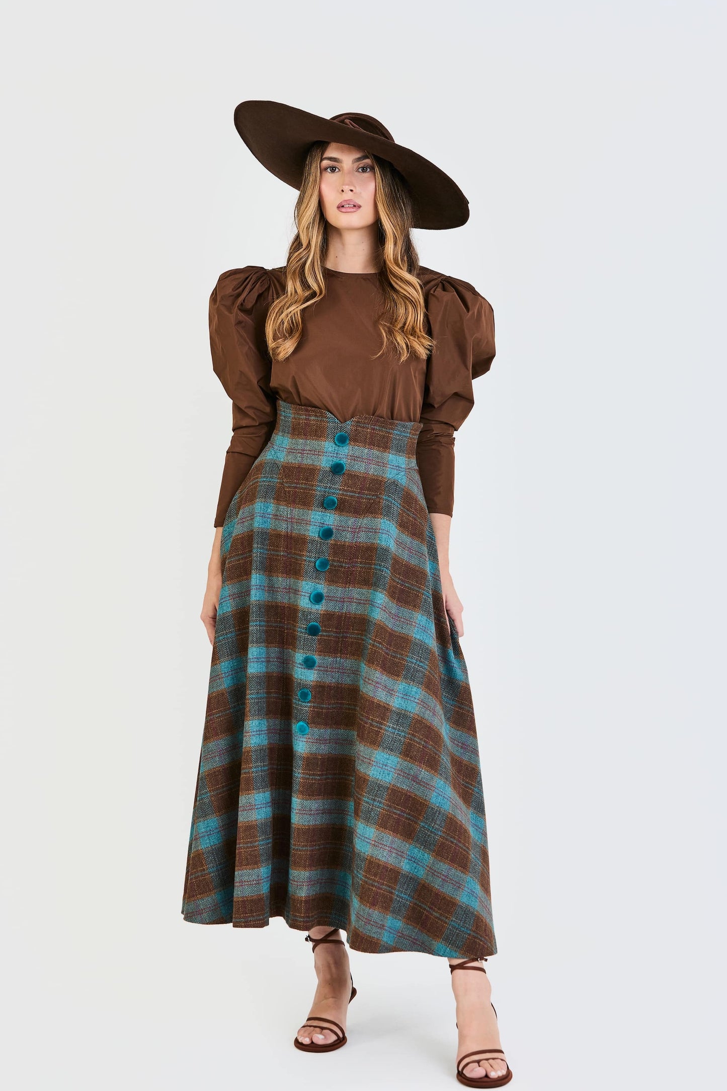 Conjunto de invitada de la colección Otoño Invierno 2025-2026 de Zinnia Brand con blusa marrón de mangas abullonadas y falda midi de cuadros en color marrón y azul. Un diseño elegante y contemporáneo pensado para bodas y eventos especiales.
