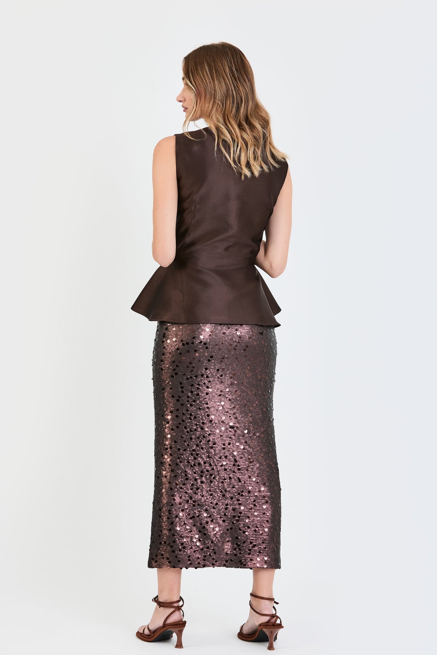 Vista de espaldas del conjunto de invitada de la colección Otoño Invierno 2025-2026 de Zinnia Brand con top estructurado en tono marrón y detalle peplum en la cintura, botones forrados  y falda de lentejuelas marrón. Un diseño elegante y contemporáneo que aporta sofisticación y feminidad.
