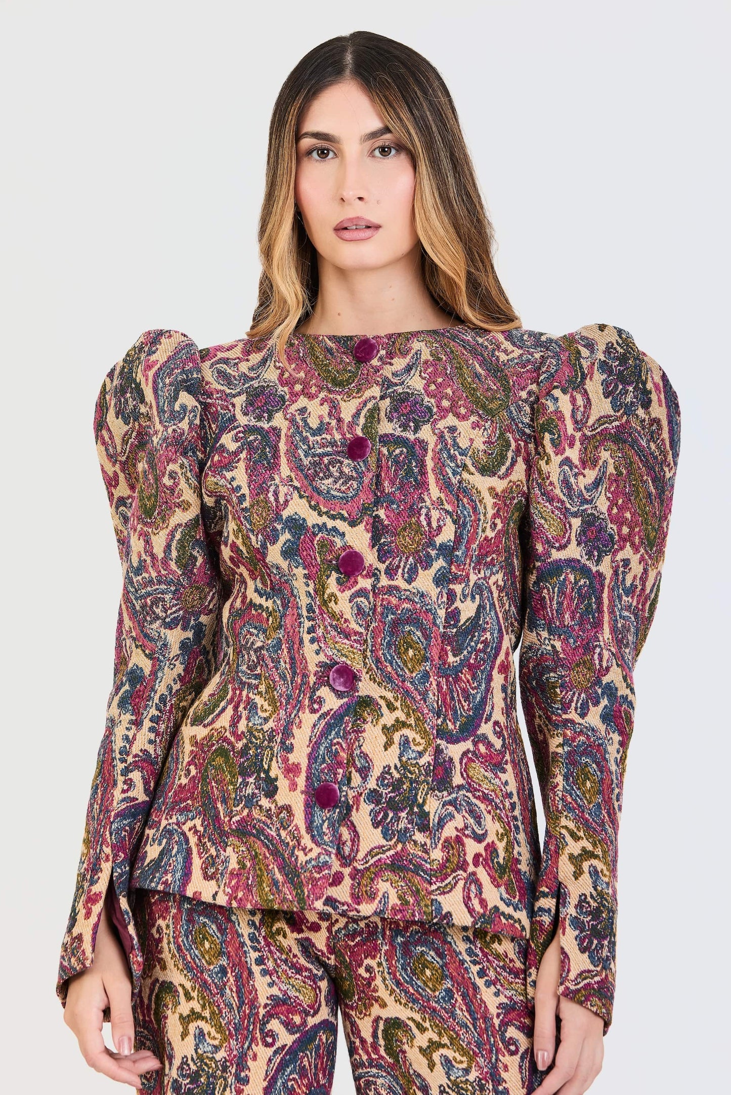 Traje de invitada de la colección Otoño Invierno 2025-2026 de Zinnia Brand con estampado cashmere en color fucsia, azul y beige. La chaqueta de cuello redondo, con botones de terciopelo magenta. Las mangas son largas y abullonadas. El pantalón es del mismo estampado de corte recto. Aporta elegancia contemporánea.
