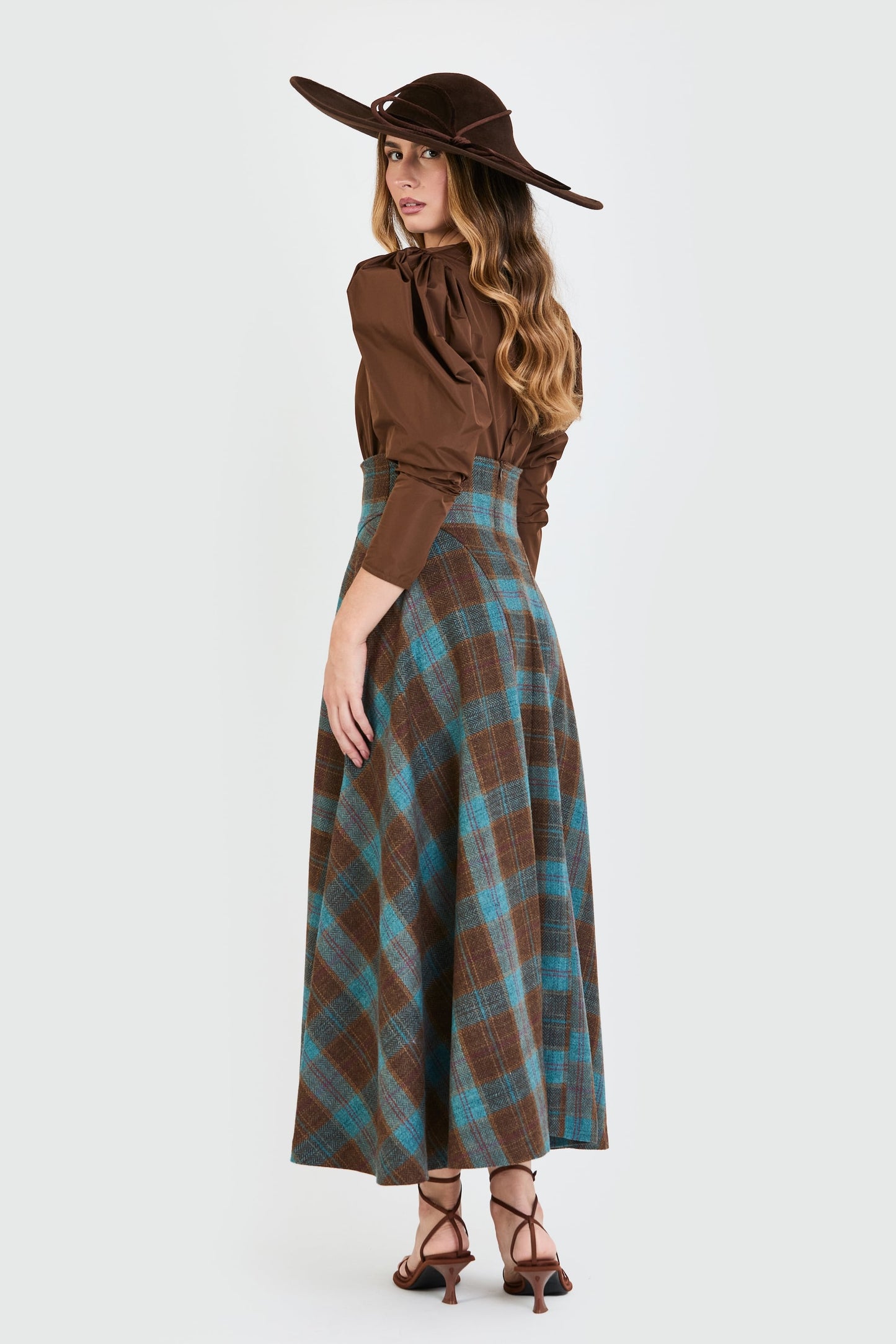 Vista lateral del conjunto de invitada de la colección Otoño Invierno 2025-2026 de Zinnia Brand con blusa marrón de mangas abullonadas y falda midi de cuadros en color marrón y azul. Un diseño elegante y contemporáneo pensado para bodas y eventos especiales.
