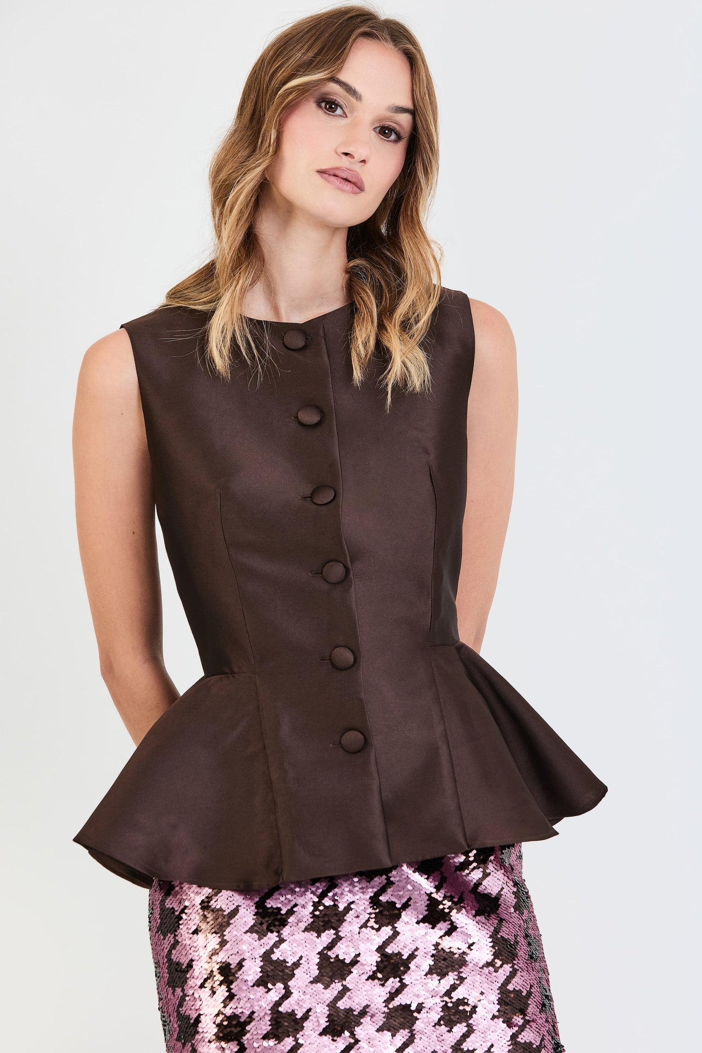  Primer plano del conjunto de invitada de la colección Otoño Invierno 2025-2026 de Zinnia Brand con top estructurado en tono marrón y detalle peplum en la cintura, botones forrados  y falda de lentejuelas estampado pata de gallo marrón y rosa. Un diseño elegante y contemporáneo que aporta sofisticación y feminidad.
