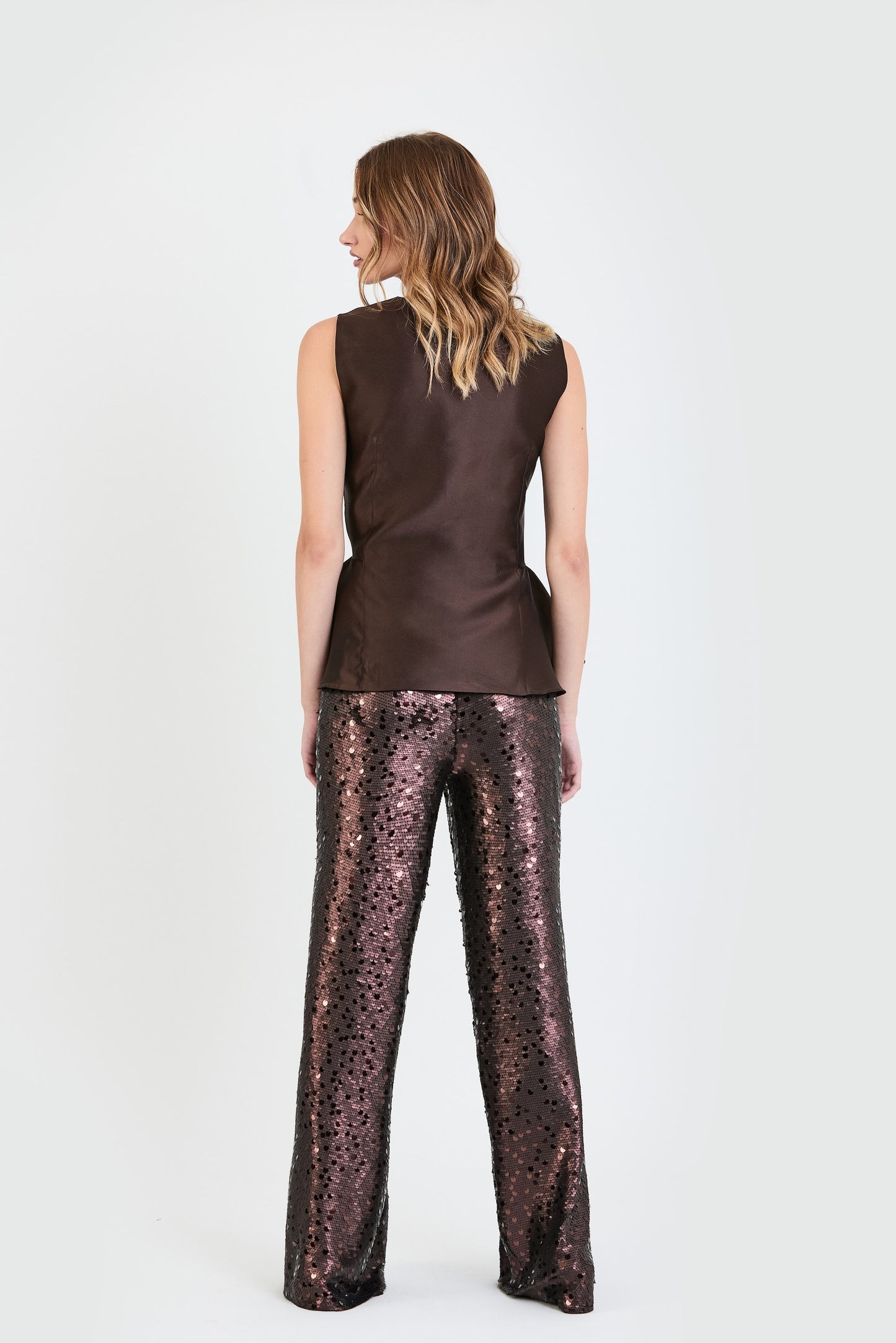 Vista de espaldas del conjunto de invitada de la colección Otoño Invierno 2025-2026 de Zinnia Brand con top estructurado en tono marrón y detalle peplum en la cintura, botones forrados  y pantalón de lentejuelas marrón. Un diseño elegante y contemporáneo que aporta sofisticación y feminidad.
