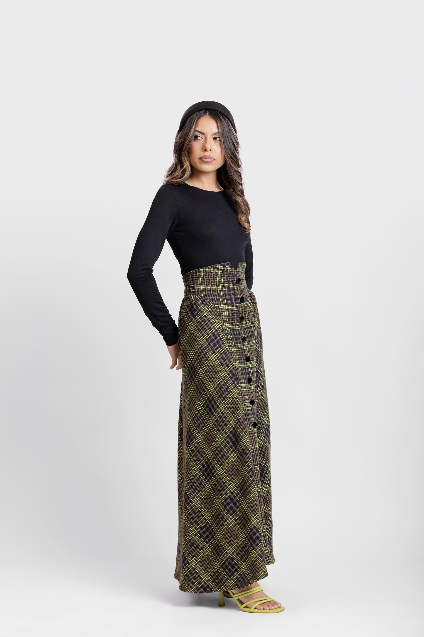 Plano  lateral de falda midi de invitada de la colección Otoño Invierno 2025-2026 de Zinnia Brand con estampado de paño de cuadros en color marino, negro y pistacho. Talle alto, realzando la figura y a la altura de la caderas sale un pequeño vuelo. Lleva una botones de terciopelo negro. Diseño elegante y contemporáneo.
