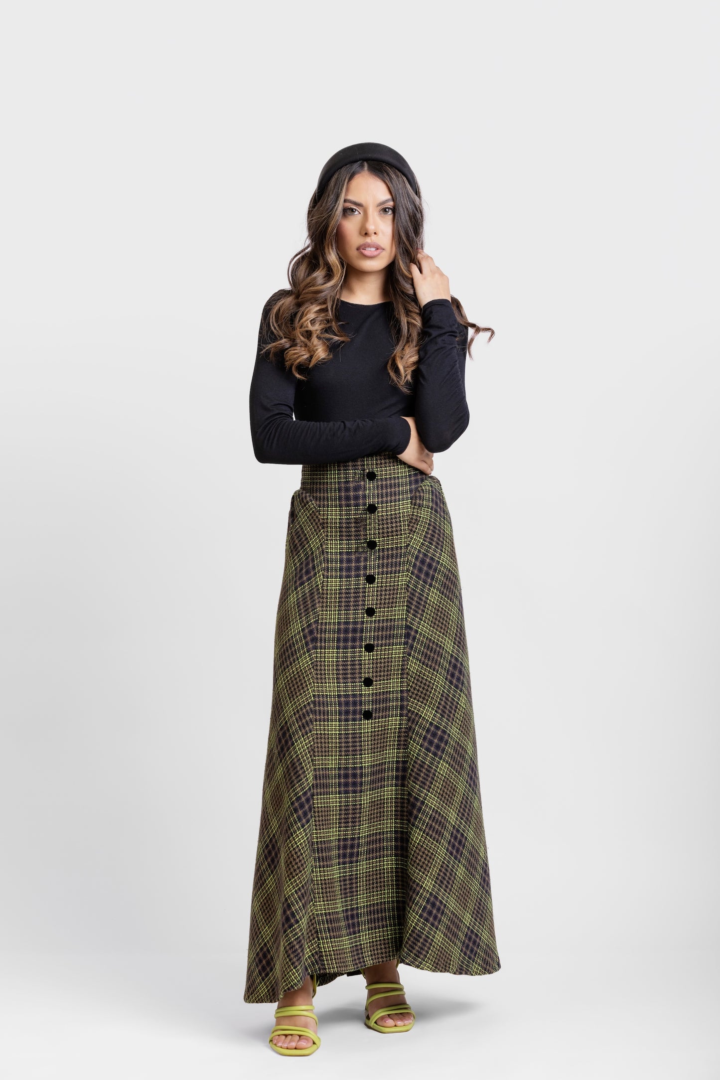 Plano  general de falda midi de invitada de la colección Otoño Invierno 2025-2026 de Zinnia Brand con estampado de paño de cuadros en color marino, negro y pistacho. Talle alto, realzando la figura y a la altura de la caderas sale un pequeño vuelo. Lleva una botones de terciopelo negro. Diseño elegante y contemporáneo.
