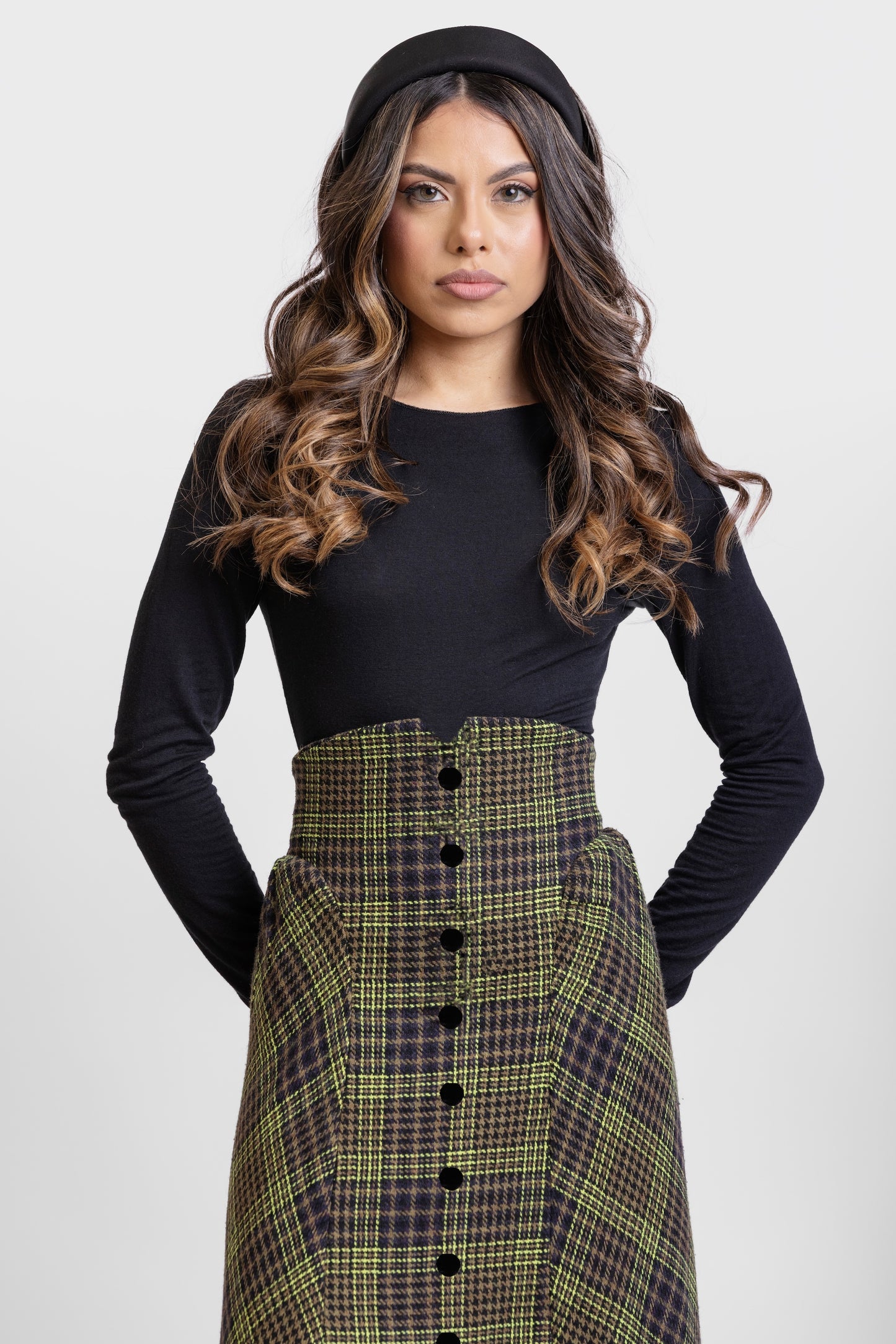 Primer plano de falda midi de invitada de la colección Otoño Invierno 2025-2026 de Zinnia Brand con estampado de paño de cuadros en color marino, negro y pistacho. Talle alto, realzando la figura y a la altura de la caderas sale un pequeño vuelo. Lleva una botones de terciopelo negro. Diseño elegante y contemporáneo.
