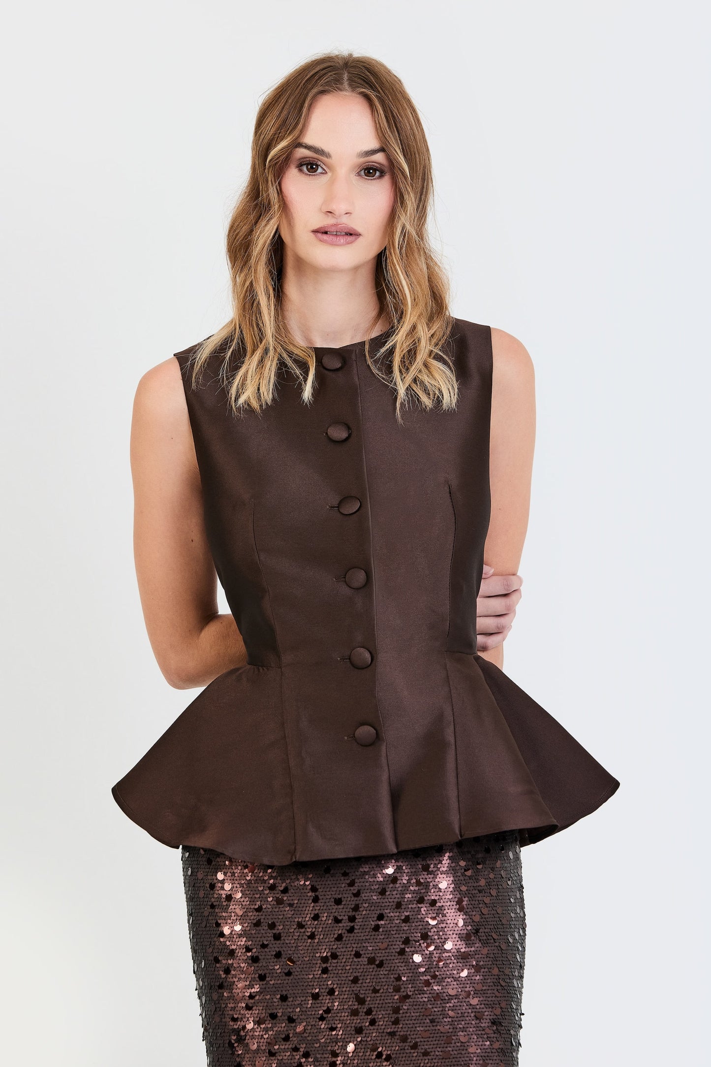 Primer plano del conjunto de invitada de la colección Otoño Invierno 2025-2026 de Zinnia Brand con top estructurado en tono marrón y detalle peplum en la cintura, botones forrados  y falda de lentejuelas marrón. Un diseño elegante y contemporáneo que aporta sofisticación y feminidad.
