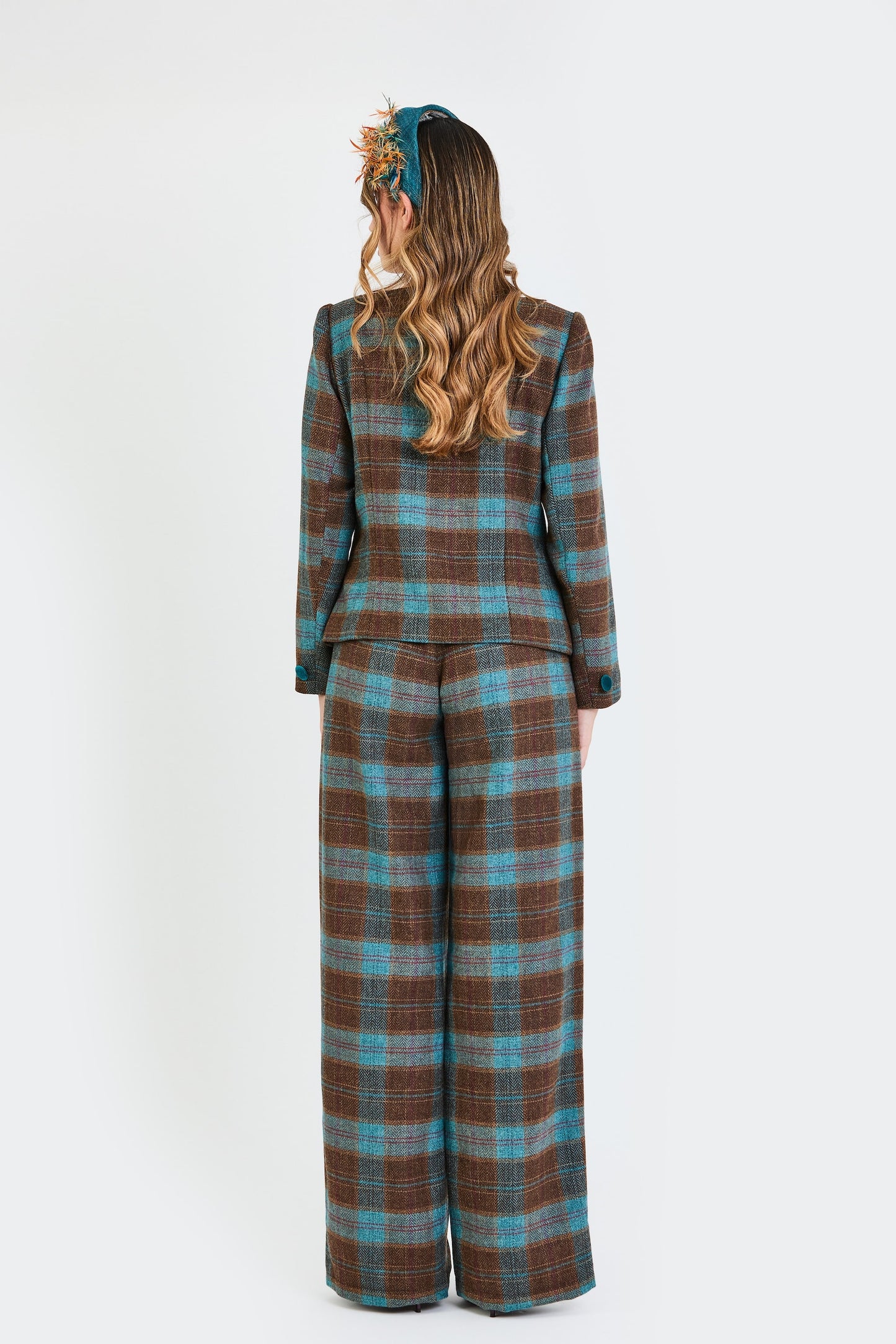 Plano de espaldas del traje de invitada de la colección Otoño Invierno 2025-2026 de Zinnia Brand con estampado de cuadros en en tonos marrón y turquesa Diseño estructurado con escote cuadrado y botones de terciopelo turquesa  y pantalón recto del mismo estampado que aporta elegancia contemporánea. 
