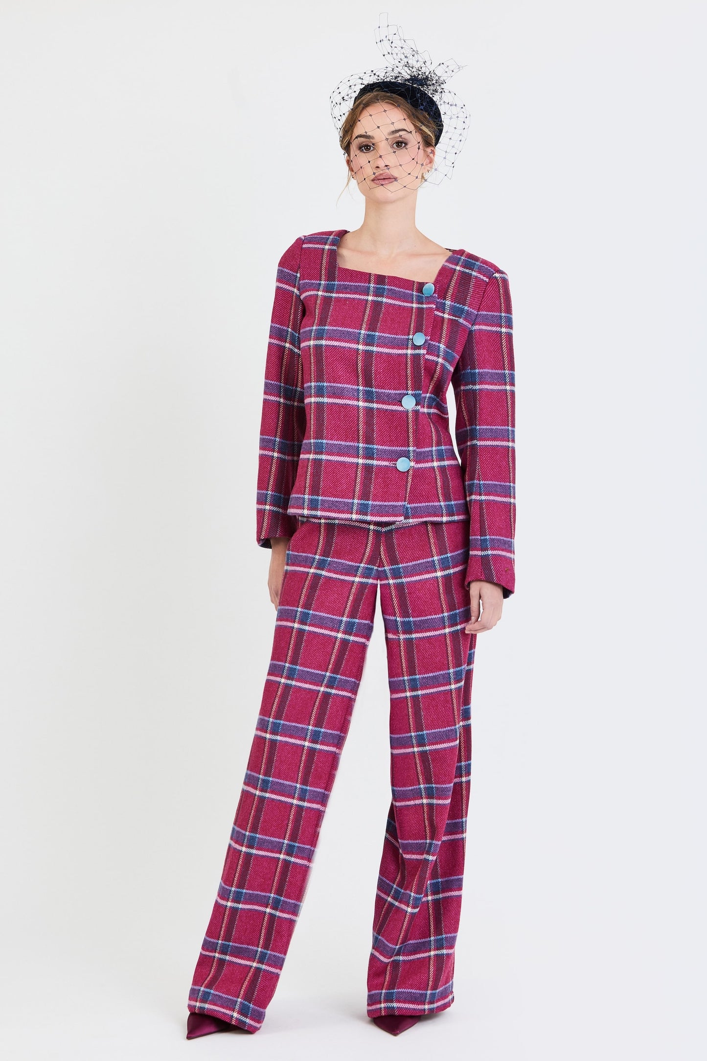 Plano  general del traje de invitada de la colección Otoño Invierno 2025-2026 de Zinnia Brand con estampado de cuadros en tonos fucsia y azul. Diseño estructurado con escote cuadrado y botones de terciopelo azul  y pantalón recto del mismo estampado que aporta elegancia contemporánea. 
