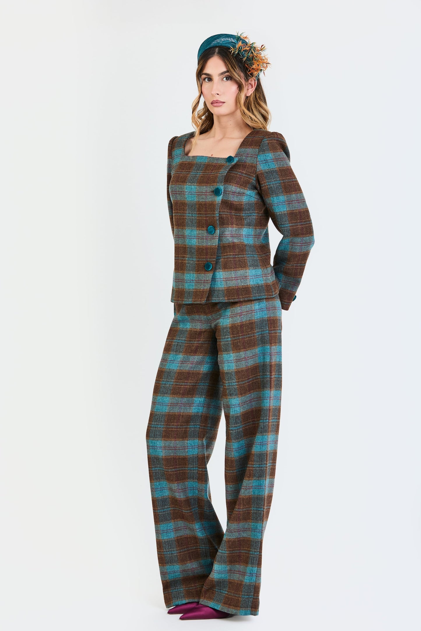 Primer plano del traje de invitada de la colección Otoño Invierno 2025-2026 de Zinnia Brand con estampado de cuadros en tonos marrón y turquesa. Diseño estructurado con escote cuadrado y botones de terciopelo turquesa y pantalón recto del mismo estampado que aporta elegancia contemporánea. 
