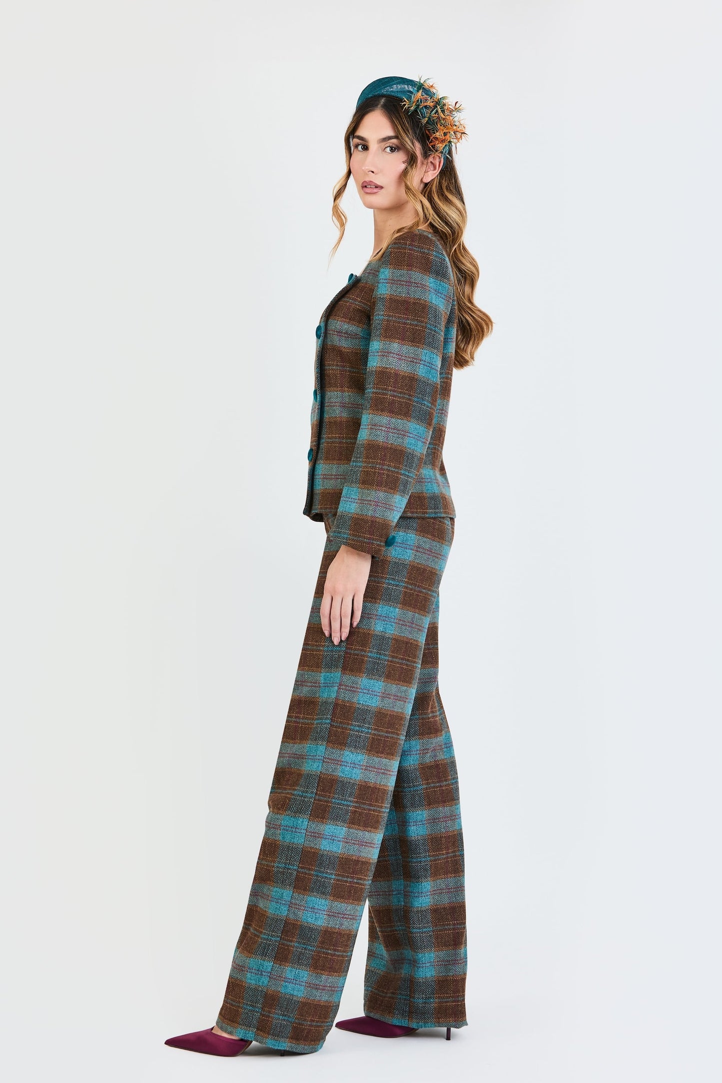 Plano lateral del traje de invitada de la colección Otoño Invierno 2025-2026 de Zinnia Brand con estampado de cuadros en tonos marrón y turquesa. Diseño estructurado con escote cuadrado y botones de terciopelo turquesa y pantalón recto del mismo estampado que aporta elegancia contemporánea. 