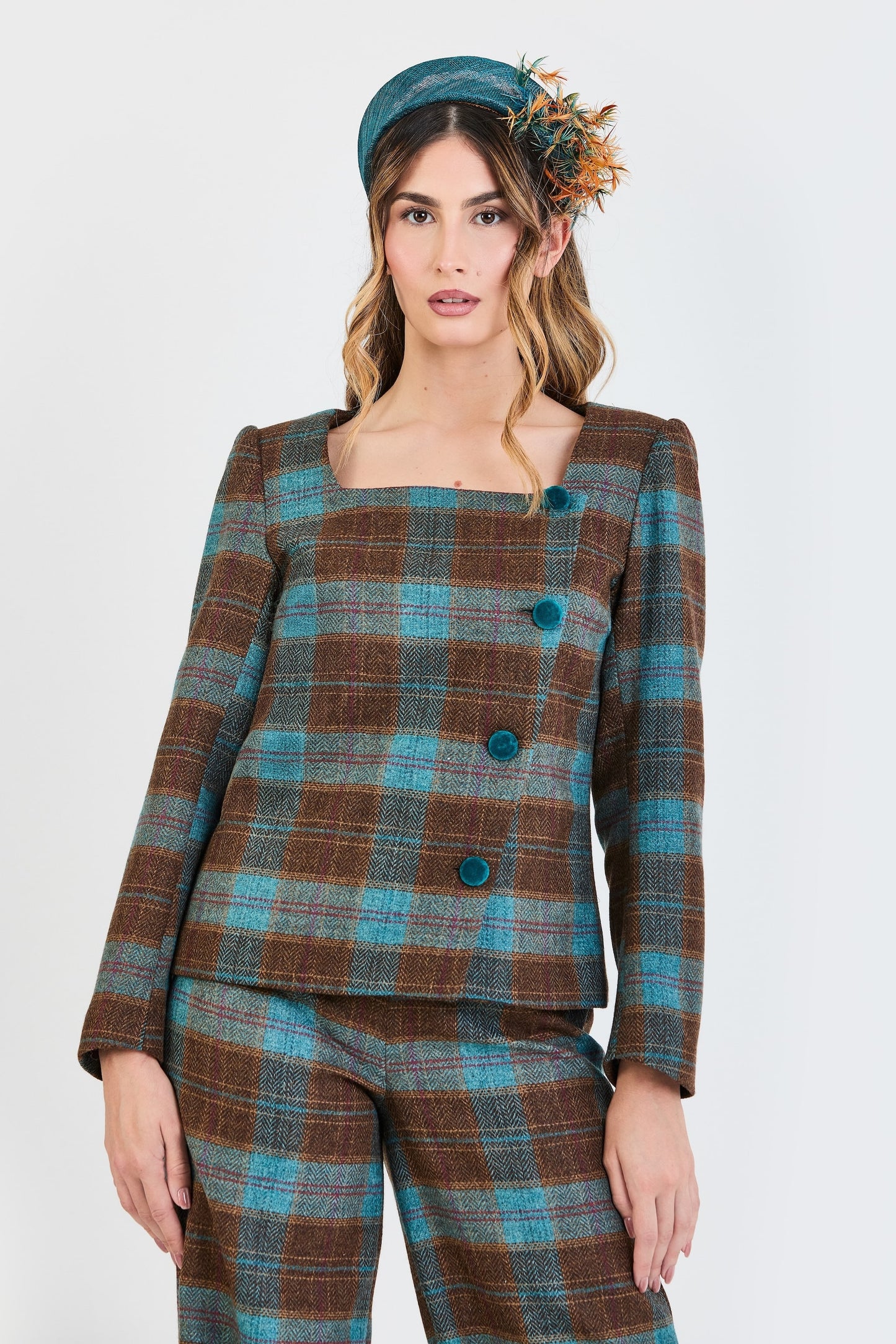 Primer plano del traje de invitada de la colección Otoño Invierno 2025-2026 de Zinnia Brand con estampado de cuadros en tonos marrón y turquesa. Diseño estructurado con escote cuadrado y botones de terciopelo turquesa.  y pantalón recto del mismo estampado que aporta elegancia contemporánea. 
